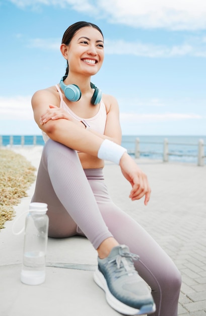 Fitness vrouw blij en strandoefening tijdens het nemen van pauze of rust terwijl ze op de promenade rent met een positieve mindset, motivatie en doel Gelukkig aziatisch atleet meisje hardloper buiten voor een training