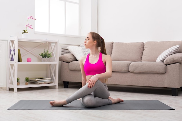 Fitness, vrouw die yoga traint in draaiende salie pose thuis. jong slank meisje maakt oefening.