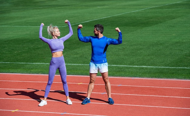 Fitness vrouw en man vieren succes of tonen biceps-spieren samen op de buitenrenbaan van het stadion met sportkleding sportsucces