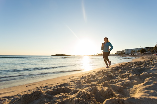 Fitness vrouw loopt door de oceaan bij zonsondergang.