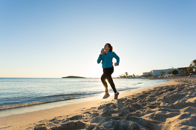 Fitness vrouw loopt door de oceaan bij zonsondergang.