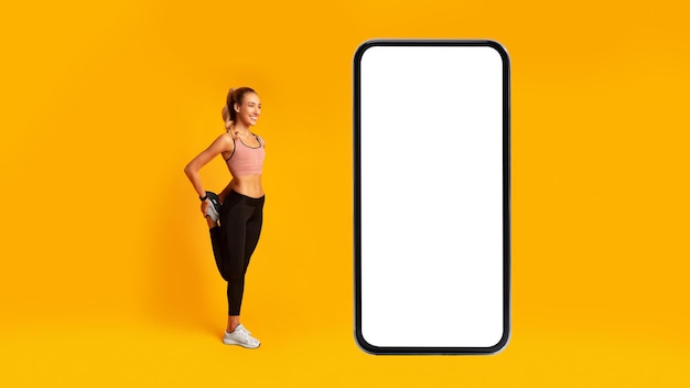 Fitness vrouw oefenen in de buurt van telefoon been uitrekken over gele achtergrond