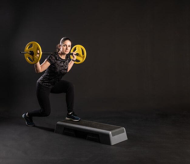 Fitness vrouw op een platform met een halter gele pannenkoeken op de bar strekt haar armen uit Ga naar binnen