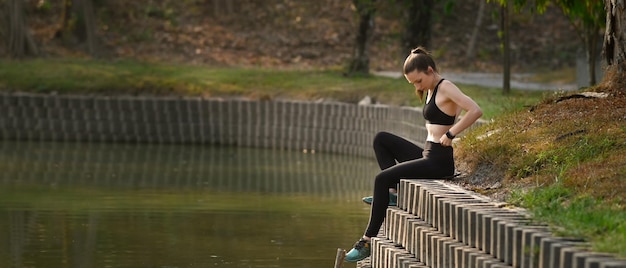 Fitness vrouw zitten in de buurt van meer rusten na succesvolle jogging oefening buitenshuis Horizontale fotobanner voor website koptekst ontwerp