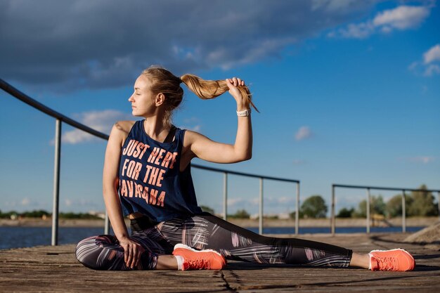 Fitness woman doing exercises on pier in sunny day