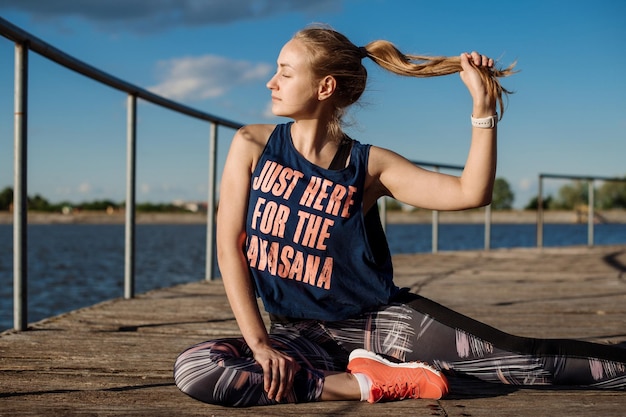 Fitness woman doing exercises on pier in sunny day