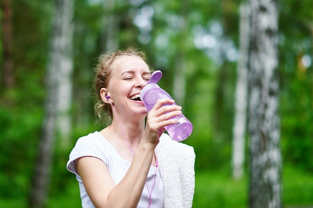 夏の公園でトレーニングを実行した後水を飲むフィットネス女性