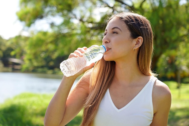 Фото Фитнес-женщина пьет воду из бутылки бразильская кавказская женщина-питьевая вода после упражнений или занятий спортом в парке