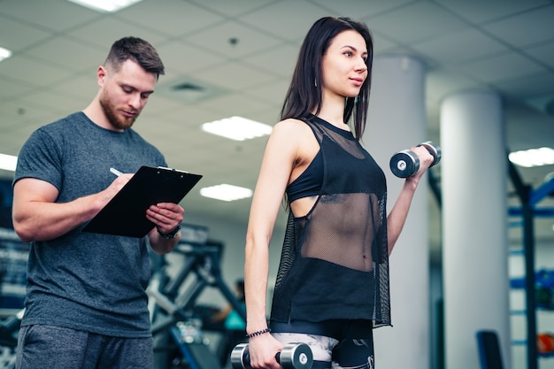 Donna di forma fisica che si esercita con l'istruttore di forma fisica in palestra.