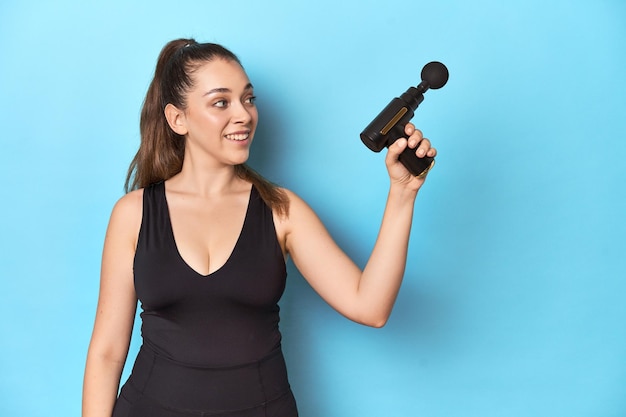 Photo fitness woman holding electric massager in a blue studio setting