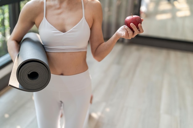 Fitness woman holding yoga mat with Fresh Apple Heathy clean vegan food before working out in yoga studio