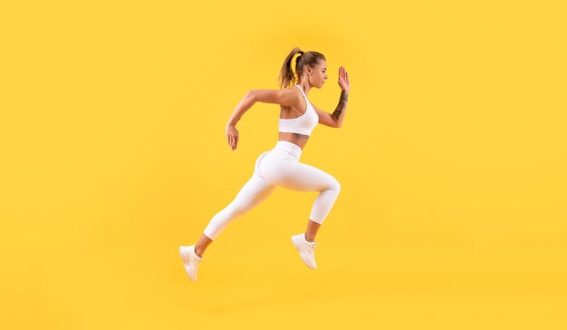 Fitness woman runner running on yellow background