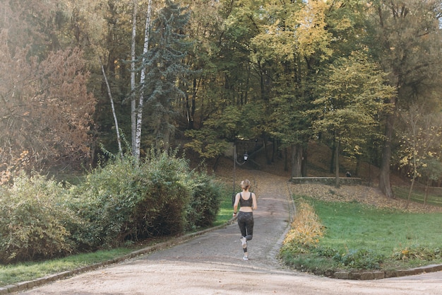 朝の公園で走っているフィットネス女性。公園の緑の草の牧草地でストレッチ運動の女性