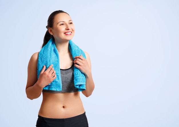 Фитнес женщина в спортивной одежде с полотенцем на плечах на синем фоне