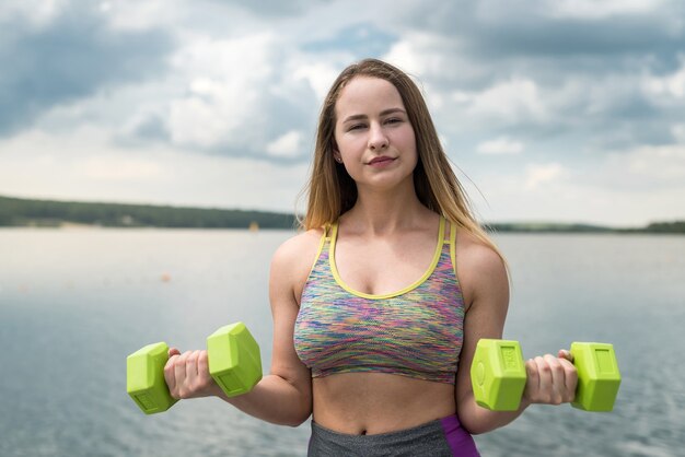 Женщина фитнеса в спортивной одежде упражнения с гантелями на открытом воздухе