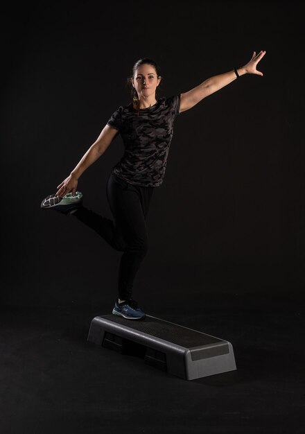 Fitness woman on step platform doing exercises Go in for sports on a black background Happy