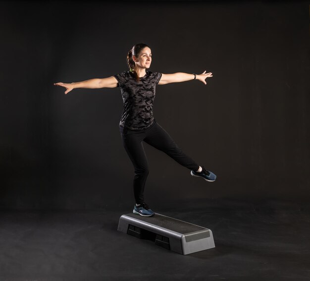 Fitness woman on step platform doing exercises Going in for sports on a black background Smiling