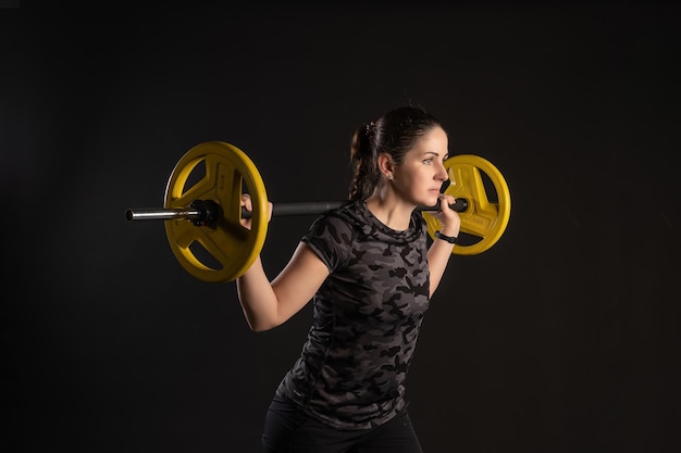 Fitness woman on a step platform with a barbell yellow pancakes pulls a leg Go in for sports on