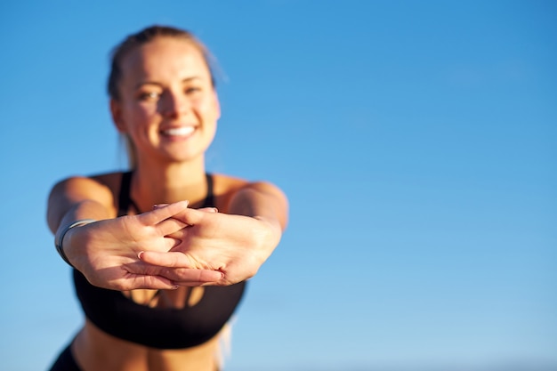 Foto donna di forma fisica che allunga le mani sul fondo del cielo blu. fa esercizi dopo aver corso. concetto di stile di vita sano.