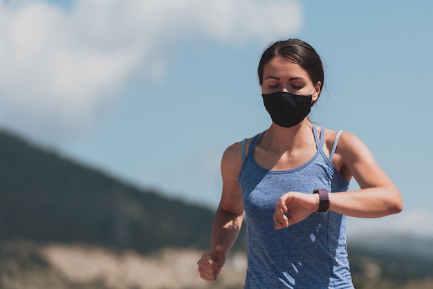 Фитнес-женщина в обтягивающей спортивной одежде в черной защитной маске бежит по городу во время вспышки коронавируса. Covid 19 и физическая активность, спорт и фитнес. Новый нормальный