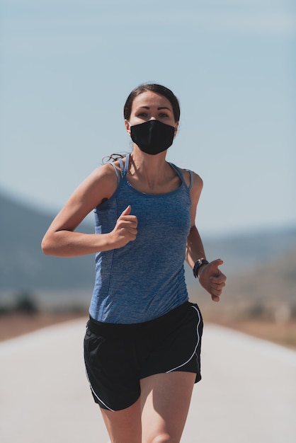 Fitness woman in tight sporty clothes wearing black protective face mask running outdoors in the city during coronavirus outbreak. Covid 19 and physical jogging activity, sport and fitness. New normal