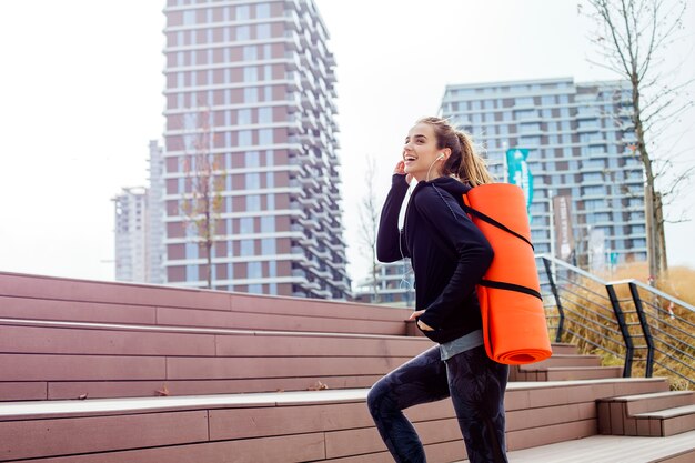 Fitness woman walking with mat on back outdoor