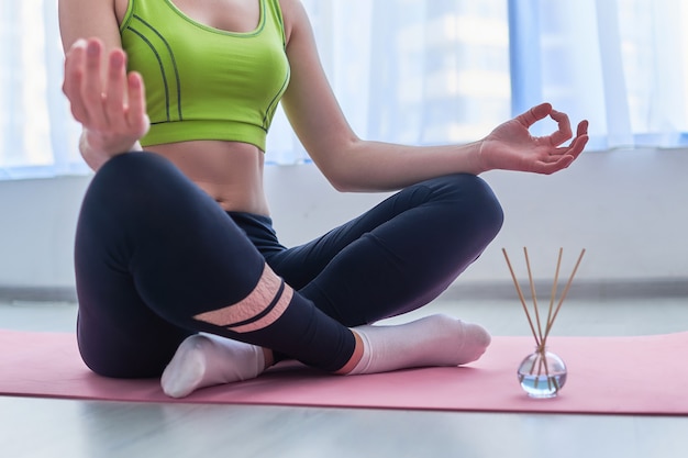 Fitness woman wearing sportswear in lotus position with aroma sticks and essential oil bottle on mat during yoga training, aromatherapy and meditation. Mental health