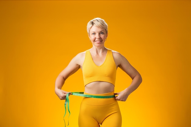 Photo fitness woman with measure tape isolated on yellow background weight loss and healthcare concept