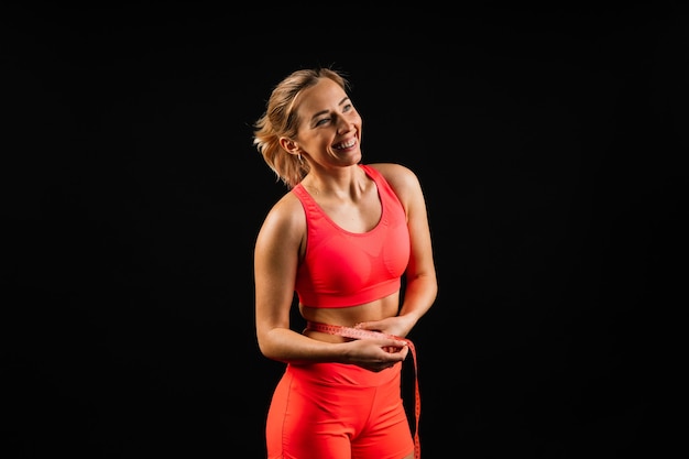 Fitness woman with tape measure showing her waist on studio background