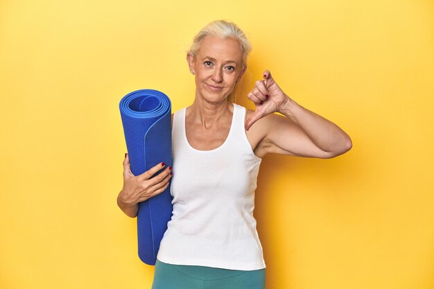 Photo fitness woman with yoga mat sportswear on yellow backdrop showing a dislike gesture thumbs down