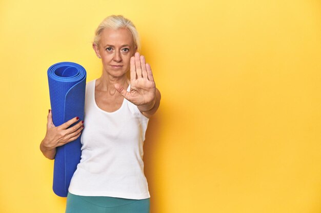 Photo fitness woman with yoga mat sportswear on yellow backdrop standing with outstretched hand