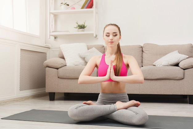 Fitness woman yoga relax meditation in lotus pose at home. Young slim girl makes exercise, copy space