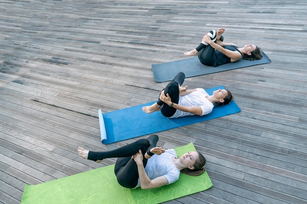 Fitness women practicing yoga exercises on yoga mat outdoors group of girls doing exercise outside