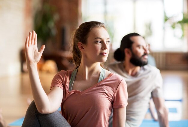 fitness, yoga and healthy lifestyle concept - woman with group of people doing half lord of the fishes pose in gym or studio