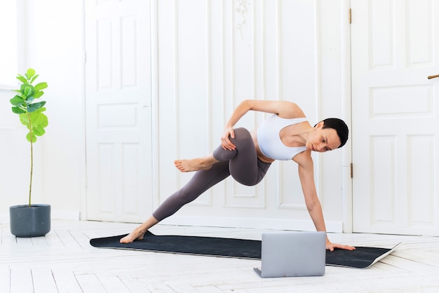 Istruttore di fitness e yoga insegna tramite laptop. formazione in linea. fit giovane donna excersising a casa, guardando il video tutorial sul computer portatile.