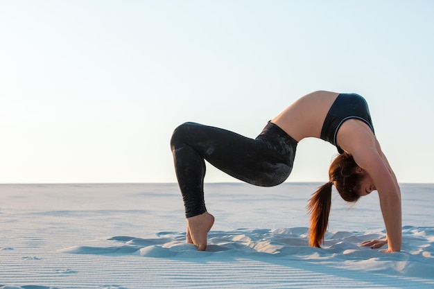 Fitness yoga woman stretching on sand. Fit female athlete doing yoga pose before running training outside in amazing landscape.