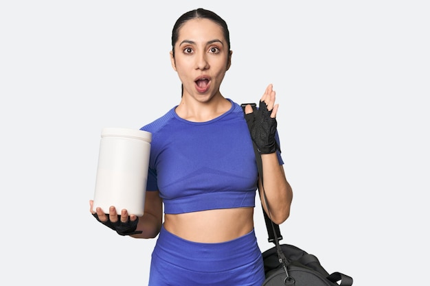 Fitness young Caucasian woman with protein and bag pointing upside with opened mouth