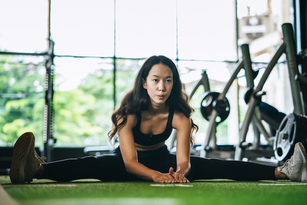 체육관 스포츠 클럽에서 바닥에 워밍업 그녀의 다리를 스트레칭 피트 니스 젊은 여자. 훈련 및 운동 개념