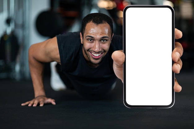 Fitnessaanbieding sportieve zwarte man die lege smartphone laat zien terwijl hij pushups doet