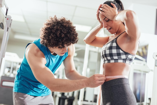 Fitnessinstructeur die de taille van een bezorgde vrouw in de sportschool meet.