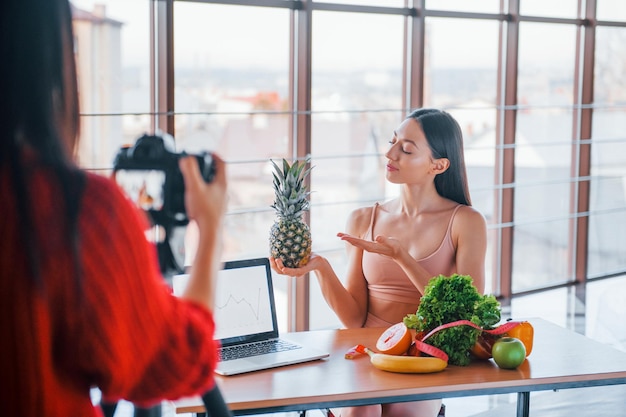 Fitnessmodel heeft fotoshoot door vrouwelijke fotograaf binnenshuis bij de tafel met gezond voedsel.