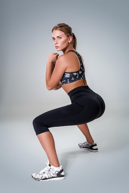 Fitnessvrouw in sportkleding die sit-ups doet om haar spieren te versterken, studioportret op grijze achtergrond