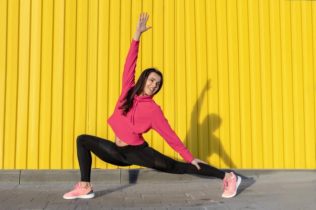 Fitnessvrouw is fitness die zich uitstrekt en buiten traint in een stedelijke omgeving met een gele muur