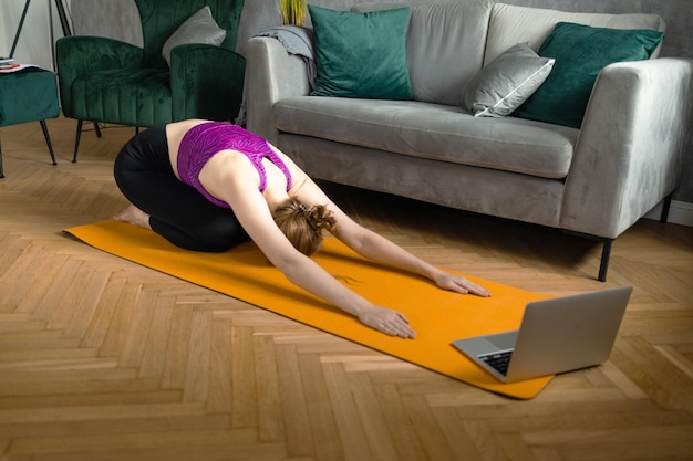 Fitte vrouw die yoga beoefent op haar mat met behulp van een online trainingsprogramma in haar tabletfitnesstechnologie