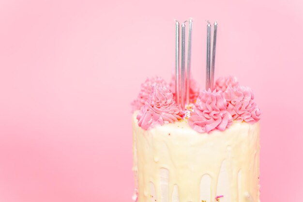 Foto cinque candeline di compleanno su torta alla crema di burro rosa e bianca con granelli rosa e gocce di ganache al cioccolato bianco.