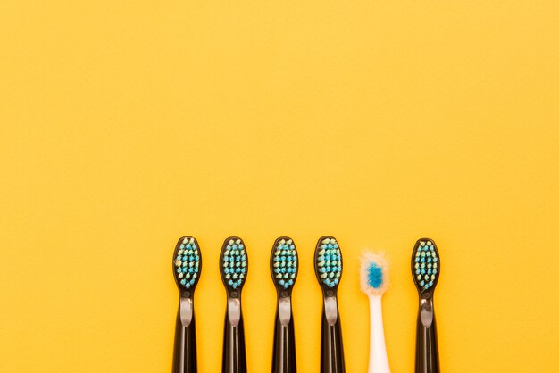 Five black new toothbrushes and one old white toothbrush on a yellow background