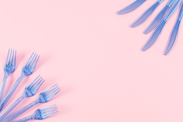 Five blue plastic transparent knives and five forks lie on the sides on a pink background