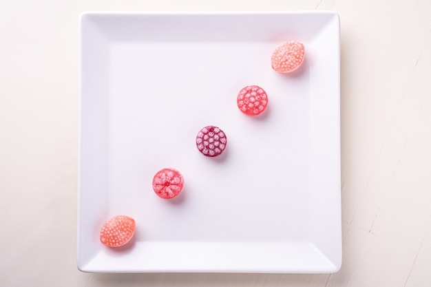 Five candy canes sweets in form of juicy berries on white plate on white background isolated, top view