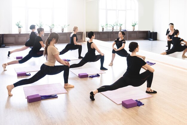 Five dancer girls warming up with stretching exercises for flexibility during class in white sports hall Active healthy lifestyle hobby recreation wellbeing weight loss concepts