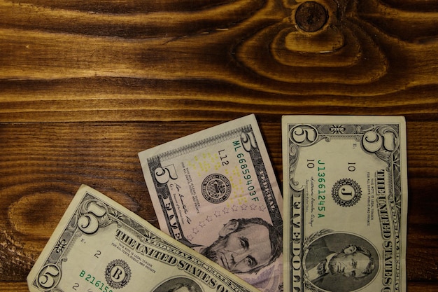 Five dollars banknotes on wooden background Top view